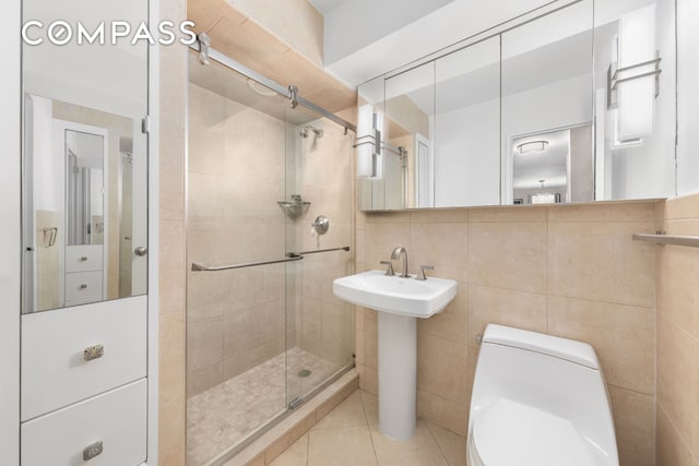 full bath featuring a shower stall, tile walls, toilet, tile patterned floors, and a sink