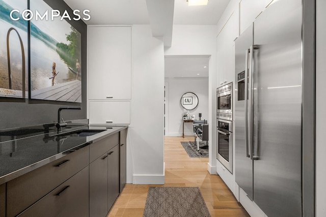 24 5th Ave Unit 824, New York City, NY 10011 - kitchen with appliances with stainless steel finishes, a sink, white cabinetry, dark stone countertops, and light wood finished floors
