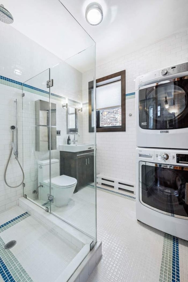 bathroom with stacked washer / dryer, a shower stall, tile patterned flooring, vanity, and a baseboard heating unit
