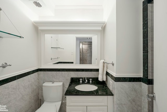 bathroom featuring tile walls, wainscoting, toilet, crown molding, and vanity
