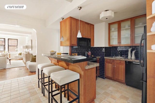 kitchen featuring black appliances, a kitchen breakfast bar, light tile patterned floors, glass insert cabinets, and backsplash