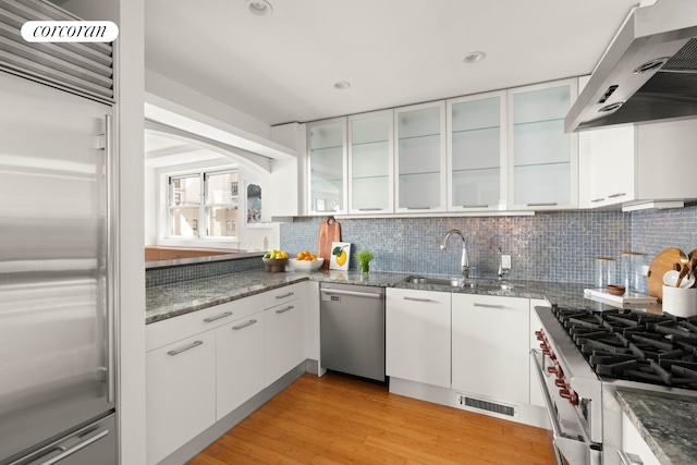 kitchen featuring high quality appliances, a sink, wall chimney range hood, white cabinetry, and tasteful backsplash