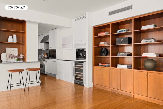 interior space with beverage cooler, open shelves, wall chimney range hood, high end stove, and light wood-type flooring