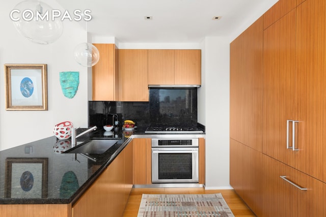 kitchen with oven, a sink, a peninsula, decorative backsplash, and dark stone countertops