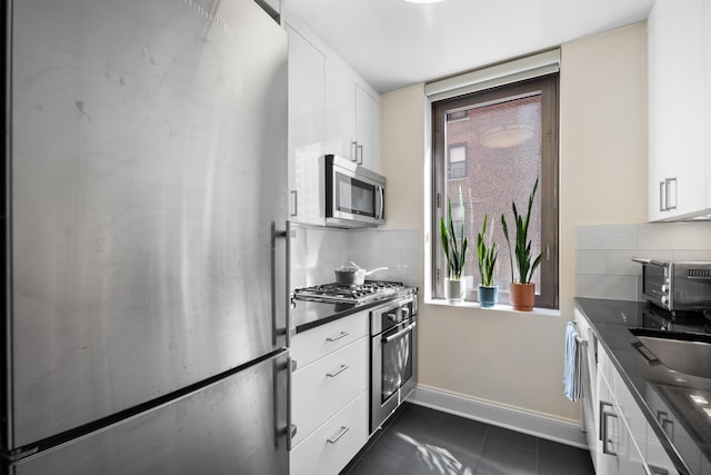 kitchen with stainless steel appliances, dark countertops, white cabinetry, and decorative backsplash