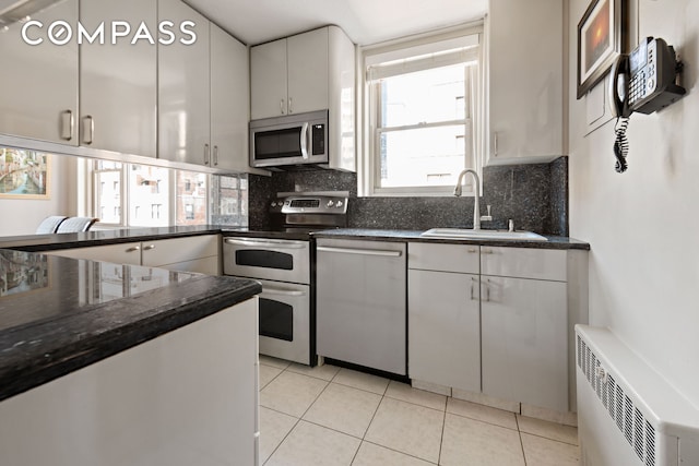 kitchen with appliances with stainless steel finishes, a sink, radiator, and light tile patterned flooring