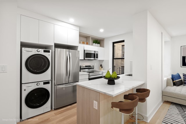 78-86 Thayer St Unit 4-G, New York City, NY 10040 - kitchen featuring appliances with stainless steel finishes, stacked washing machine and dryer, modern cabinets, light wood-style floors, and a breakfast bar