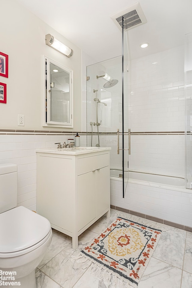 bathroom featuring marble finish flooring, toilet, tiled shower / bath, vanity, and tile walls