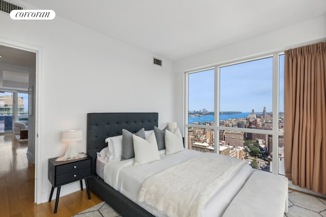 bedroom featuring light wood-style flooring, multiple windows, a city view, and a water view