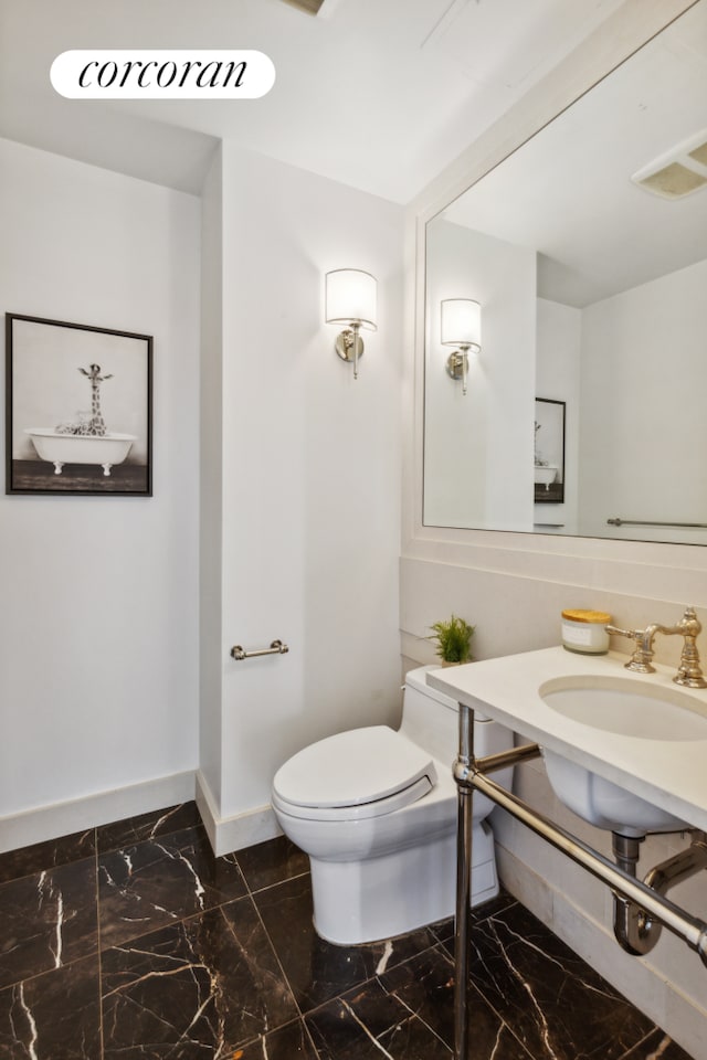 half bath featuring baseboards, marble look tile flooring, toilet, and a sink