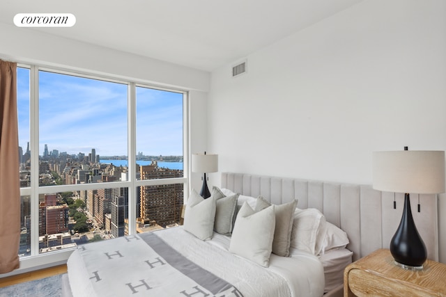 bedroom featuring multiple windows, a skyline view, a water view, and wood finished floors
