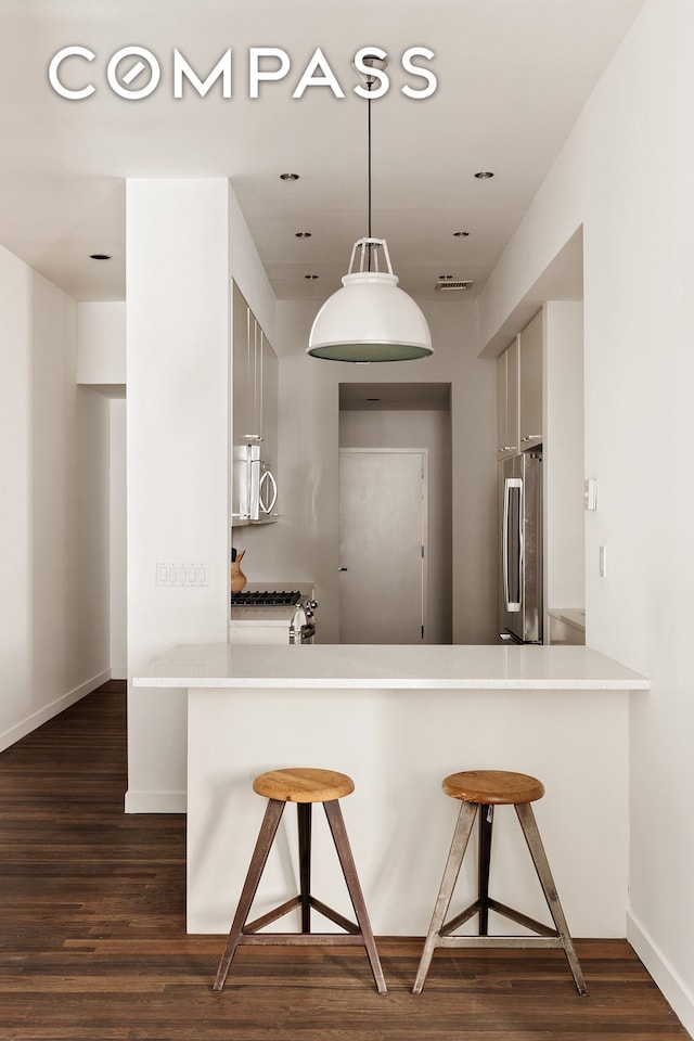 kitchen with appliances with stainless steel finishes, a kitchen breakfast bar, dark wood-style floors, light countertops, and recessed lighting