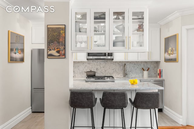 kitchen with appliances with stainless steel finishes, a sink, tasteful backsplash, white cabinetry, and light wood-style flooring