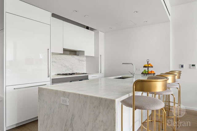 kitchen with a sink, white cabinetry, modern cabinets, a kitchen bar, and wood finished floors