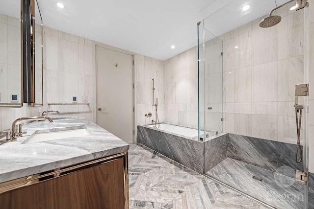 bathroom with tiled shower, a tub with marble appearance, tile walls, double vanity, and marble tiled floors
