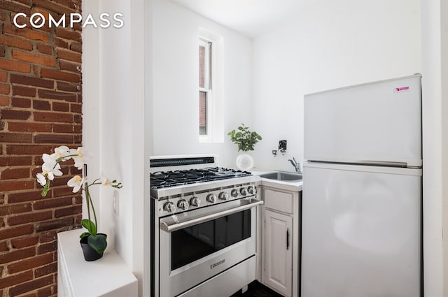 15 Jones St Unit 5H, New York City, NY 10014 - kitchen featuring freestanding refrigerator, high end stainless steel range, a sink, brick wall, and light countertops