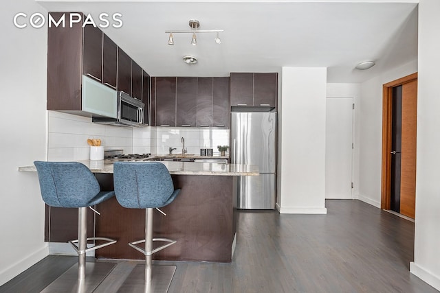 502 9th Ave Unit 4A, New York City, NY 10018 - kitchen with stainless steel appliances, a peninsula, dark brown cabinets, dark wood-type flooring, and baseboards