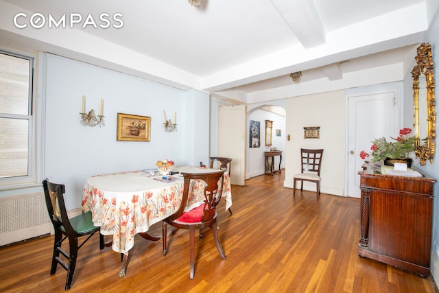 dining area featuring arched walkways, wood finished floors, beamed ceiling, and radiator
