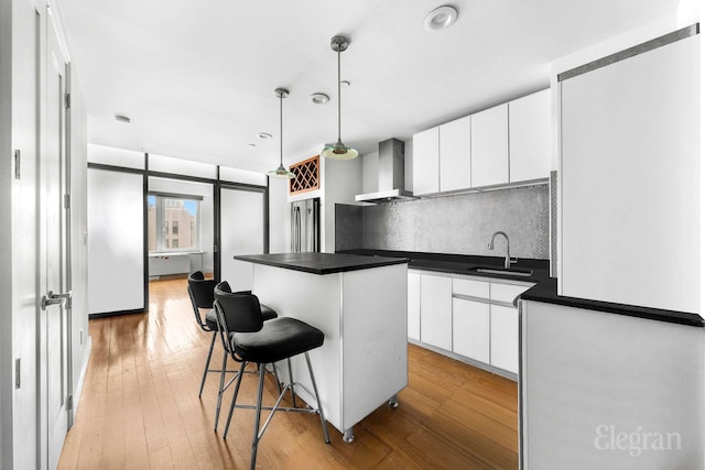 kitchen with wall chimney range hood, a sink, dark countertops, a kitchen island, and decorative backsplash