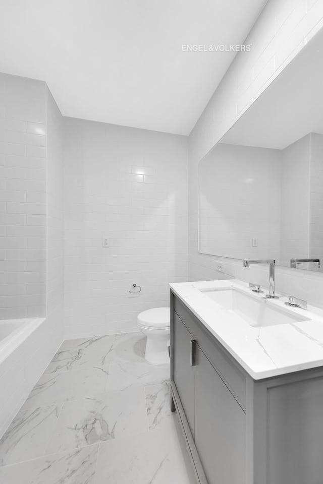 bathroom with toilet, vanity, marble finish floors, and a bathtub