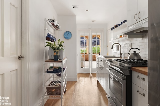 kitchen featuring stainless steel range with gas cooktop, wooden counters, a sink, wood finished floors, and backsplash