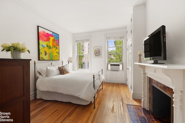 bedroom featuring crown molding, wood-type flooring, cooling unit, a fireplace with flush hearth, and baseboards