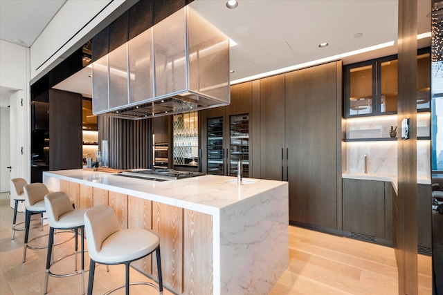 460 W 42nd St Unit Ph-1C, New York City, NY 10036 - kitchen featuring light stone countertops, modern cabinets, light wood finished floors, stainless steel gas stovetop, and a breakfast bar area