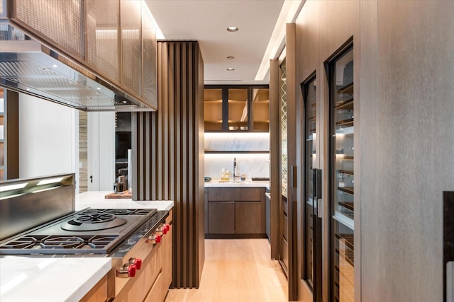 460 W 42nd St Unit Ph-1C, New York City, NY 10036 - kitchen featuring stovetop with downdraft, wall chimney range hood, a sink, glass insert cabinets, and light wood-style flooring