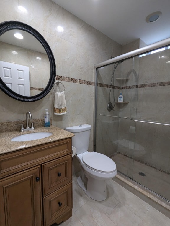 bathroom featuring a stall shower, toilet, vanity, and tile walls