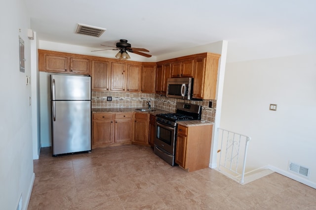 kitchen featuring stainless steel appliances, a sink, ceiling fan, decorative backsplash, and brown cabinets