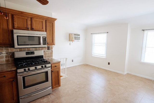 kitchen featuring appliances with stainless steel finishes, decorative backsplash, brown cabinets, dark stone countertops, and baseboards