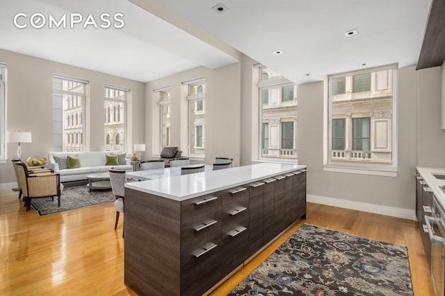 kitchen featuring dark brown cabinets, light countertops, light wood-type flooring, modern cabinets, and baseboards