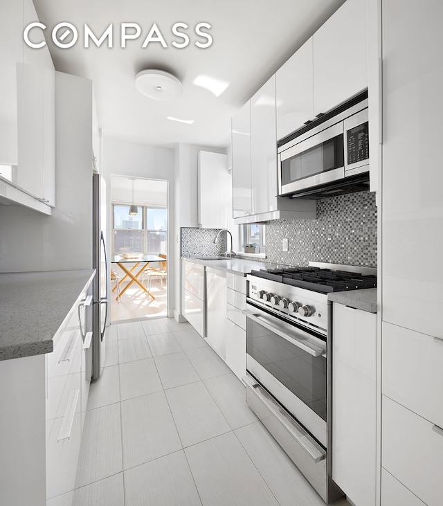 kitchen featuring appliances with stainless steel finishes, decorative backsplash, white cabinetry, modern cabinets, and a sink