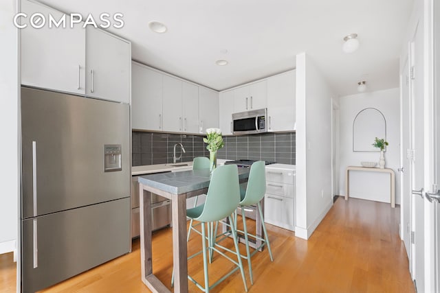 139 Skillman Ave Unit 7B, New York City, NY 11211 - kitchen featuring appliances with stainless steel finishes, white cabinets, light wood finished floors, backsplash, and recessed lighting