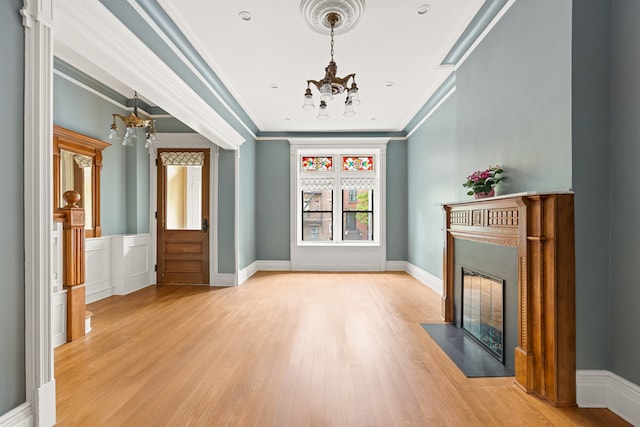 unfurnished living room with a chandelier, light wood finished floors, a fireplace with flush hearth, crown molding, and baseboards