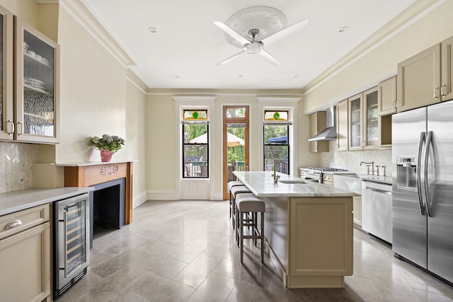 kitchen with stainless steel appliances, wine cooler, wall chimney range hood, a sink, and decorative backsplash