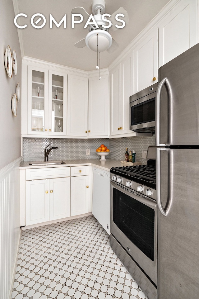 kitchen with appliances with stainless steel finishes, a sink, light countertops, white cabinetry, and a wainscoted wall