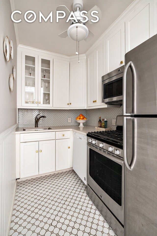 311 E 71st St Unit 2B, New York City, NY 10021 - kitchen with appliances with stainless steel finishes, a sink, light countertops, white cabinets, and a wainscoted wall