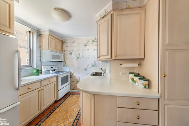 kitchen with white appliances, a sink, light brown cabinetry, light countertops, and wallpapered walls