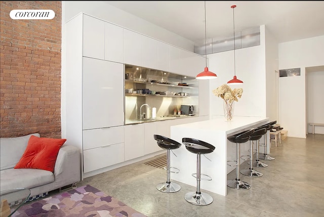 192 Water St Unit 1W, New York City, NY 11201 - kitchen with concrete flooring, modern cabinets, a breakfast bar, white cabinets, and brick wall