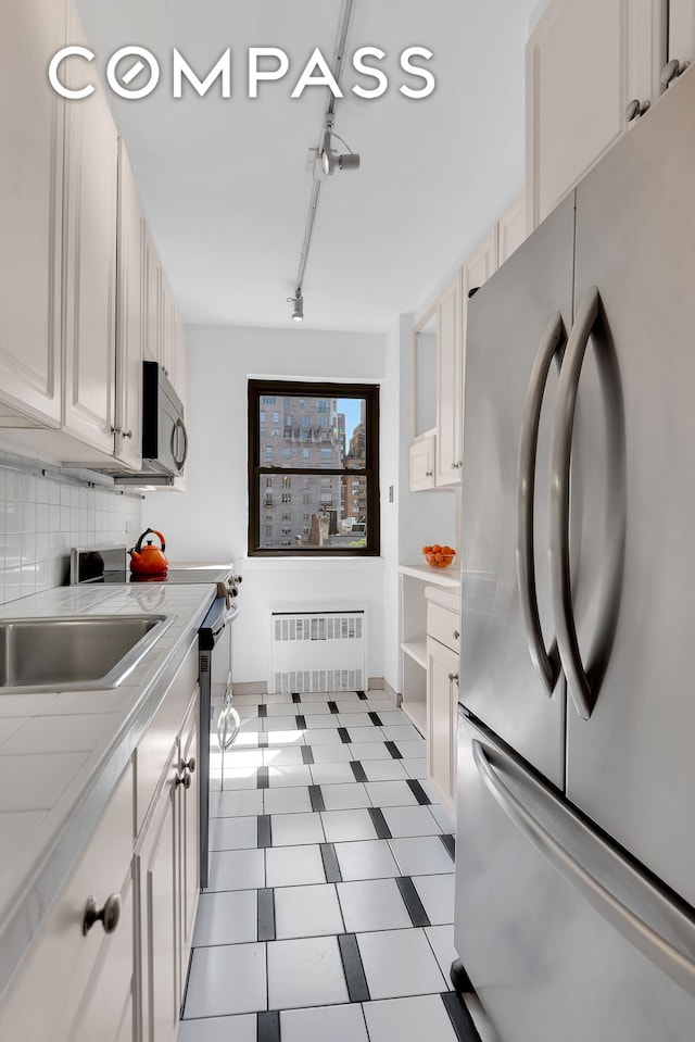 120 E 81st St Unit 8A, New York City, NY 10028 - kitchen featuring stainless steel appliances, radiator heating unit, light countertops, backsplash, and white cabinetry