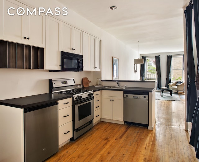 kitchen with stainless steel appliances, dark countertops, a peninsula, and light wood-type flooring