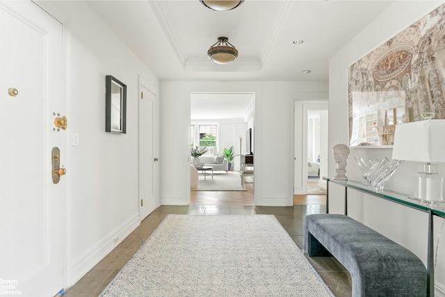 corridor with tile patterned floors, ornamental molding, a raised ceiling, and baseboards