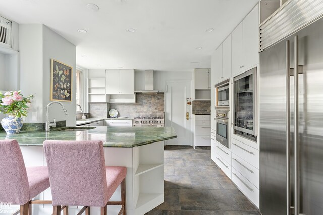 607 W End Ave Unit 4A, New York City, NY 10024 - kitchen with appliances with stainless steel finishes, open shelves, wall chimney exhaust hood, a sink, and stone finish flooring