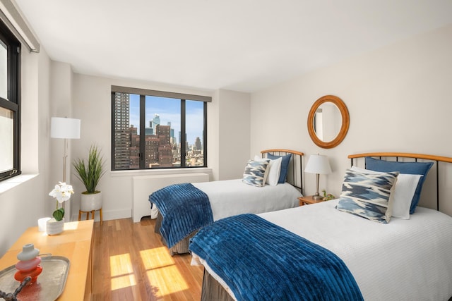 bedroom with radiator, wood finished floors, and baseboards