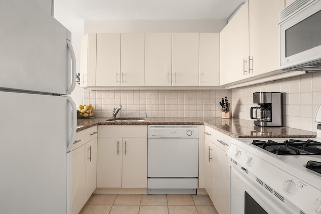 kitchen with white appliances, a sink, dark stone counters, decorative backsplash, and light tile patterned flooring