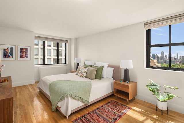 bedroom featuring wood finished floors, baseboards, and a city view