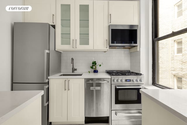 kitchen featuring appliances with stainless steel finishes, a sink, tasteful backsplash, and white cabinets