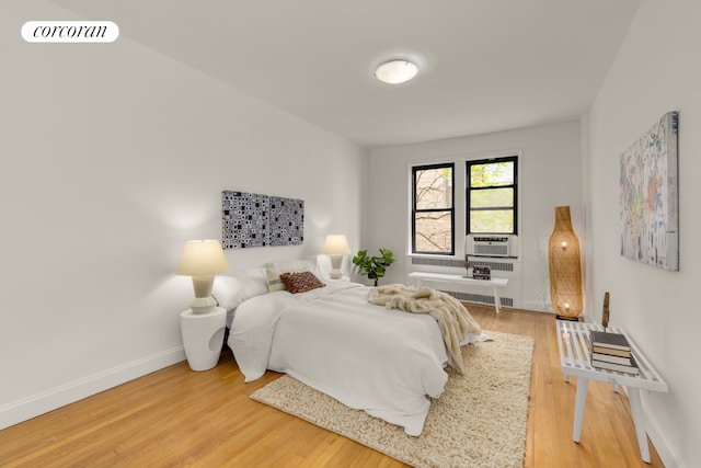 bedroom with radiator, light wood-style floors, cooling unit, and baseboards