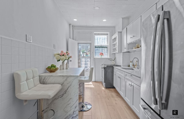 kitchen with appliances with stainless steel finishes, a sink, white cabinetry, open shelves, and light wood-style floors
